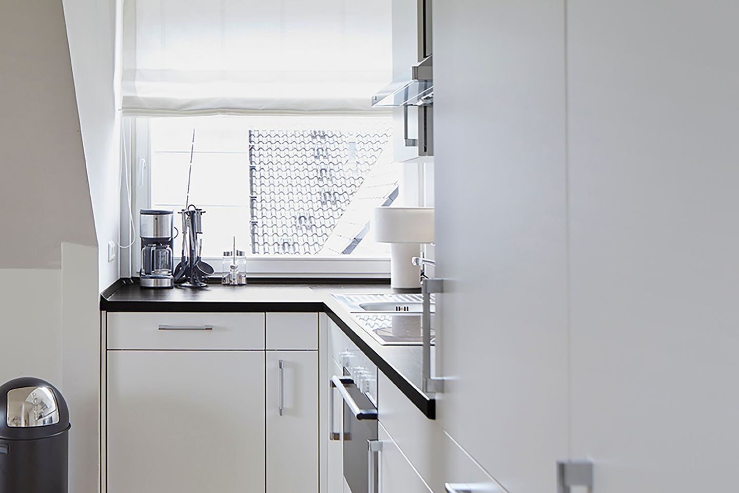 Una cocina moderna con armarios blancos, una cafetera y un ventanal con vistas a un tejado de baldosas.