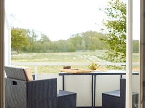 Ein Balkon mit Korbstühlen und einem Tisch, mit Blick auf eine Wiese und Bäume.