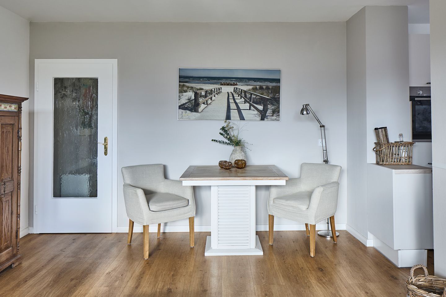 Ein Essbereich mit zwei Stühlen, einem Tisch und einem Bild mit Strandmotiv.