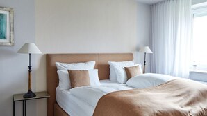 A neatly made bed with white and brown bedding, two bedside lamps, and a framed picture on the wall. - Experience relaxation at TECHTs Apartmenthaus StrandPerle on Timmendorfer Strand (Timmendorfer Strand)