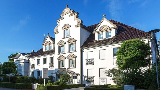 A large, white, multi-story building with a symmetrical facade, a central tower, and a red-tiled roof. - Experience relaxation at TECHTs Apartmenthaus StrandPerle on Timmendorfer Strand (Timmendorfer Strand)