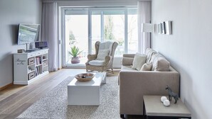 A modern living room with a sofa, armchair, coffee table, and a television on a stand. - Experience relaxation at TECHTs Apartmenthaus StrandPerle on Timmendorfer Strand (Timmendorfer Strand)