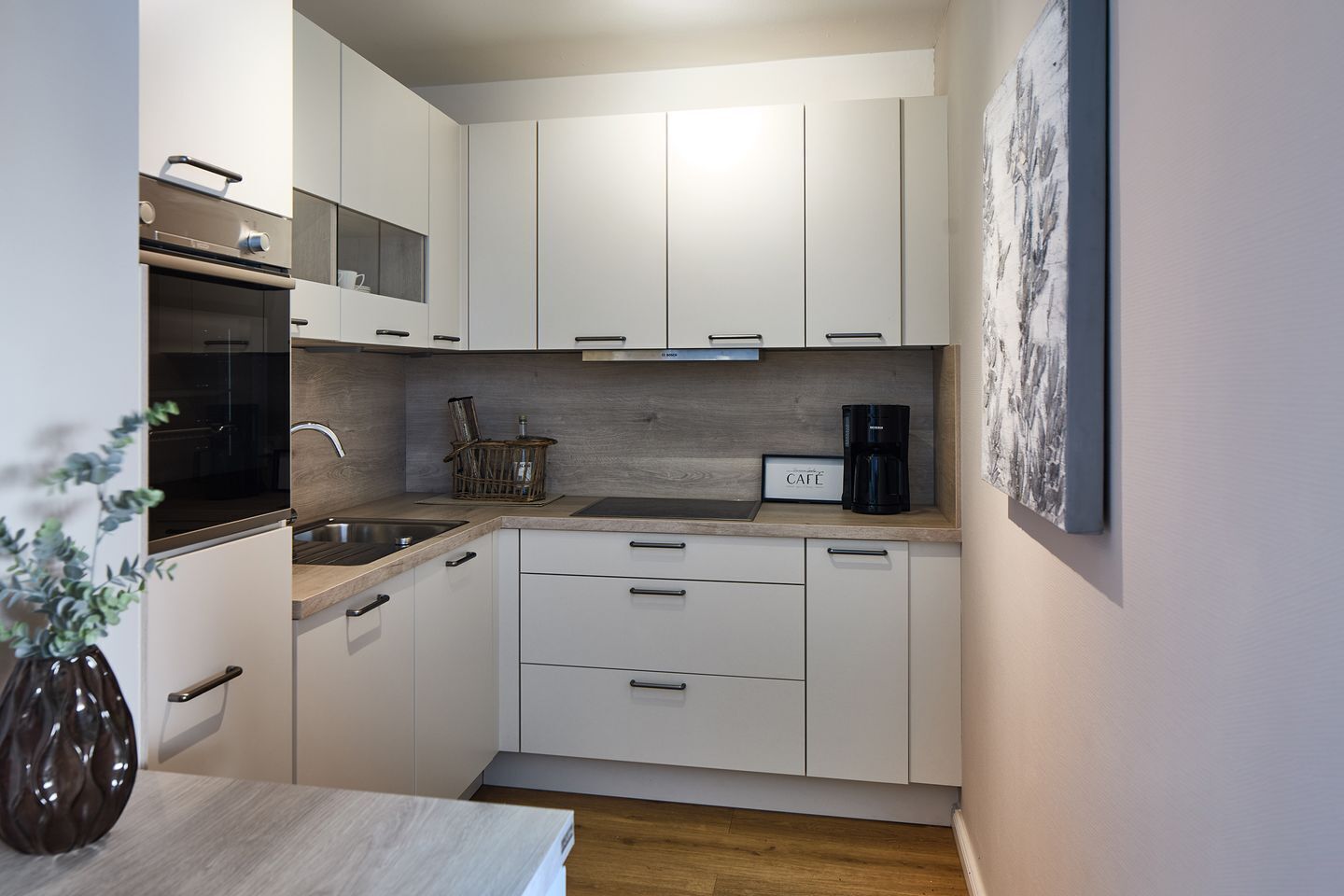 A compact kitchen with white cabinets, a built-in oven, a coffee maker, and a small sink.