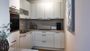 A compact kitchen with white cabinets, a built-in oven, a coffee maker, and a small sink.