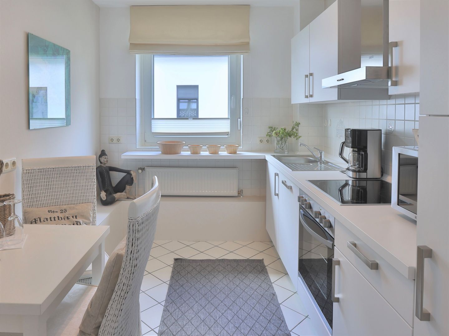 A modern kitchen with white cabinetry, a built-in oven, a coffee maker, and a window with a view.
