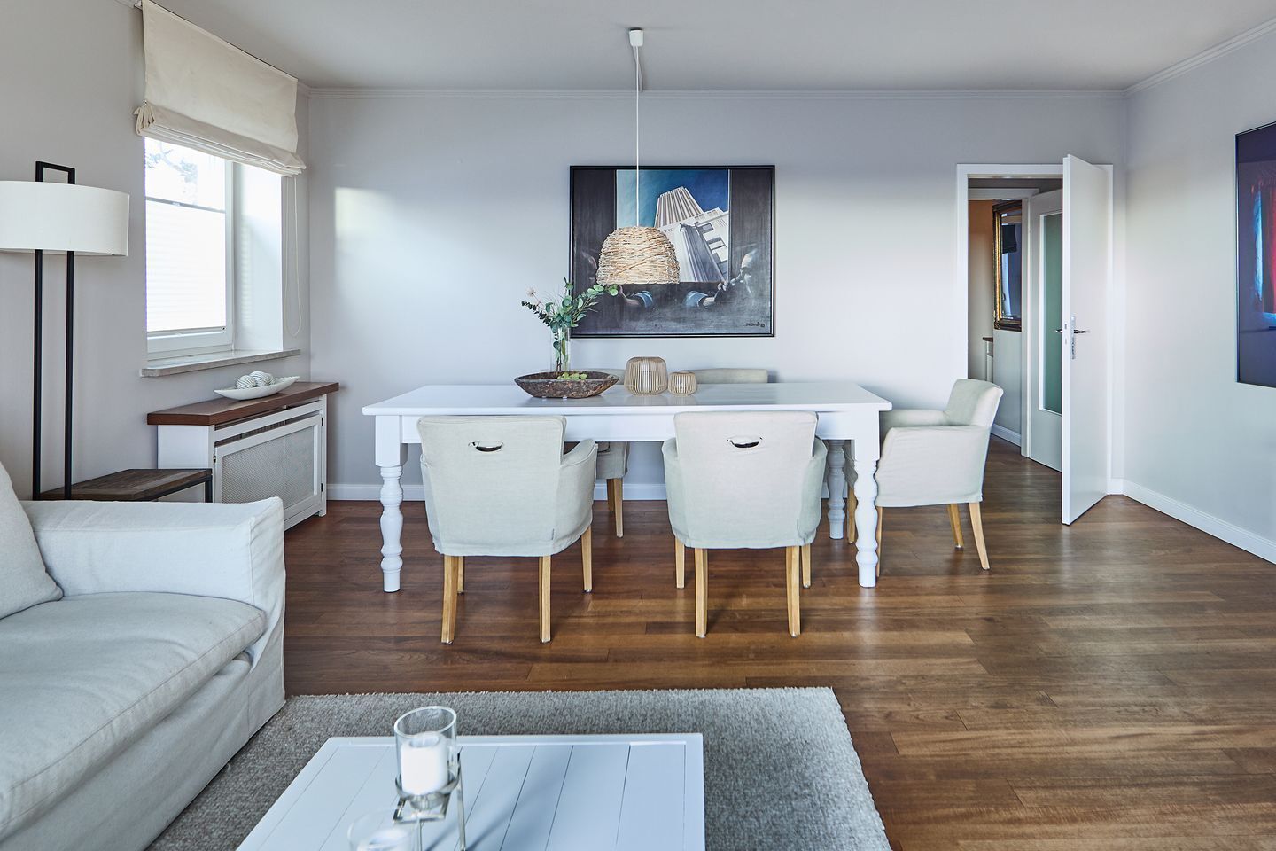 Ein modernes Wohnzimmer mit einem weißen Sofa, einem Esstisch mit vier Stühlen und einem Couchtisch mit einem Glas und einer Kerze.