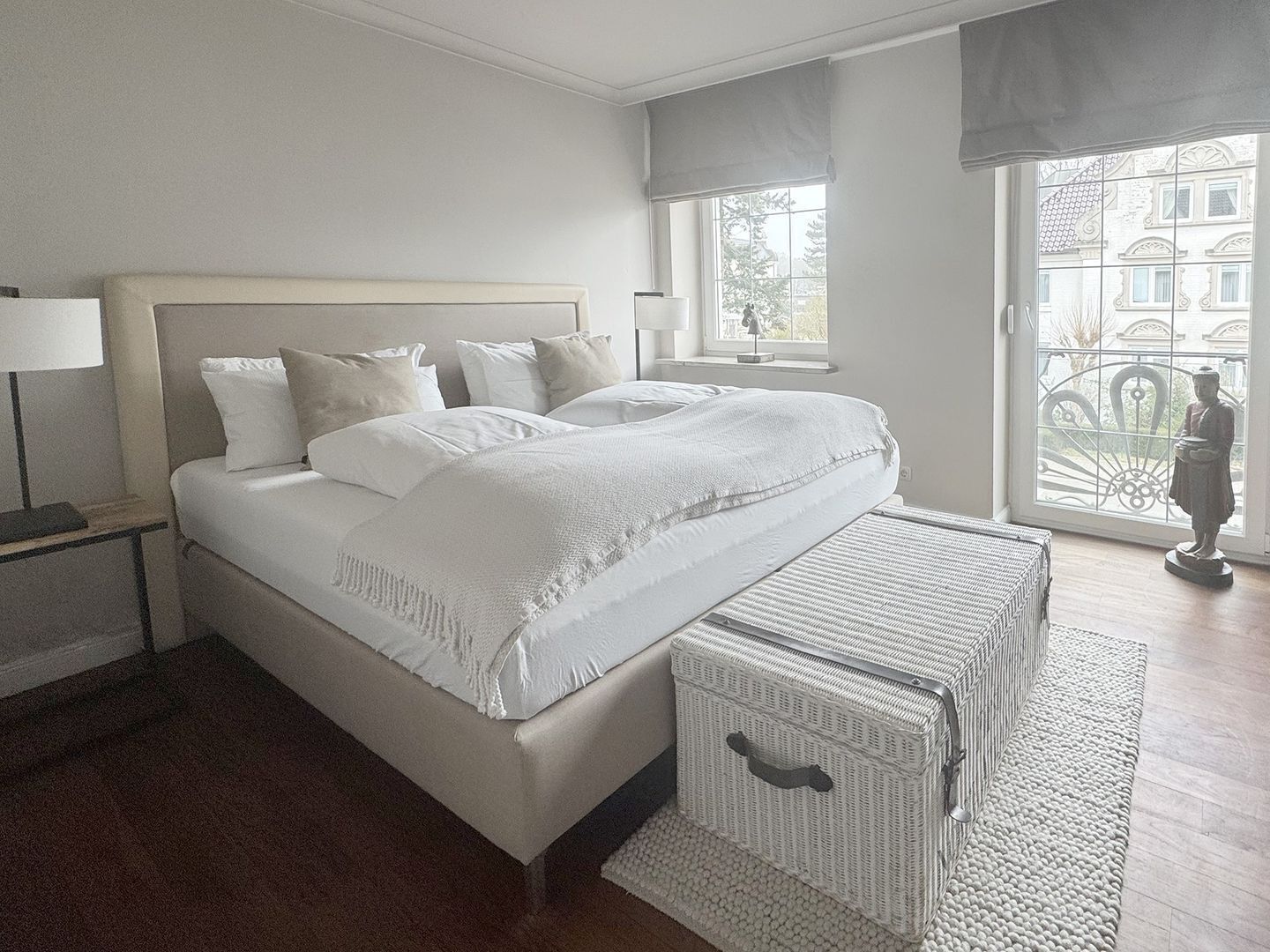 A bedroom with a bed, a nightstand, a window with a view, and a statue.
