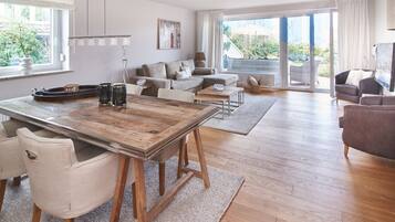 Een ruime woonkamer met een houten eettafel, comfortabele zithoek en grote ramen met uitzicht op de omgeving.