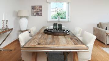 A dining area with a wooden table, white chairs, a vase with plants, and a painting on the wall.