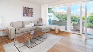 Ein modernes Wohnzimmer mit einer Eckcouch, einem Couchtisch aus Holz und einer großen Schiebeglastür, die in einen Garten führt.