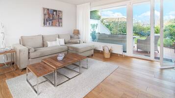 Een moderne woonkamer met een hoekbank, een houten salontafel en een grote schuifdeur naar een tuin.