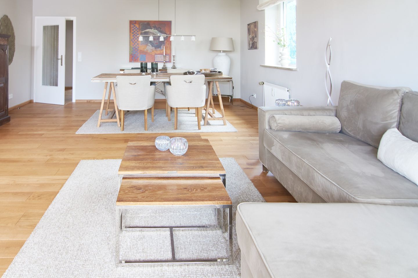 Een moderne woonkamer met een houten salontafel, een grijze bank en een eethoek met een tafel en stoelen.