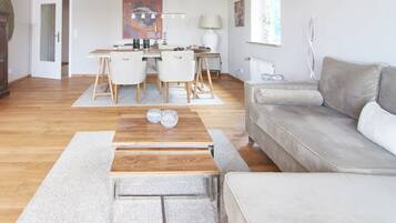 Een moderne woonkamer met een houten salontafel, een grijze bank en een eethoek met een tafel en stoelen.
