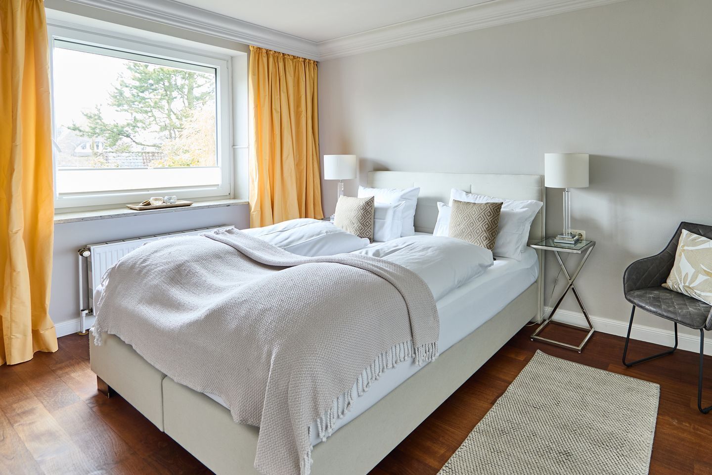 Ein ordentlich eingerichtetes Schlafzimmer mit einem großen Bett, Nachttischen und Blick ins Freie durch ein Fenster.