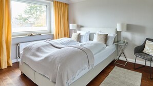 A neatly arranged bedroom with a large bed, bedside tables, and a view of the outdoors through a window. - Welcome to TECHTS - TECHTs Apartmenthaus (Timmendorfer Strand)