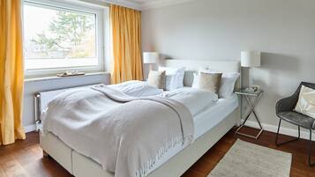 Ein ordentlich eingerichtetes Schlafzimmer mit einem großen Bett, Nachttischen und Blick ins Freie durch ein Fenster.