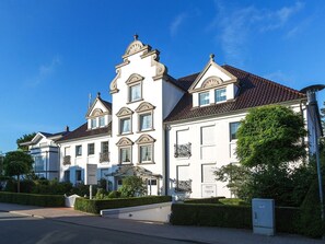 A large, white, multi-story building with a symmetrical facade, a central tower, and a red-tiled roof. - "Meerzeit" maisonette apartment - stylish living at Timmendorfer Platz - TECHTs (Timmendorfer Strand)