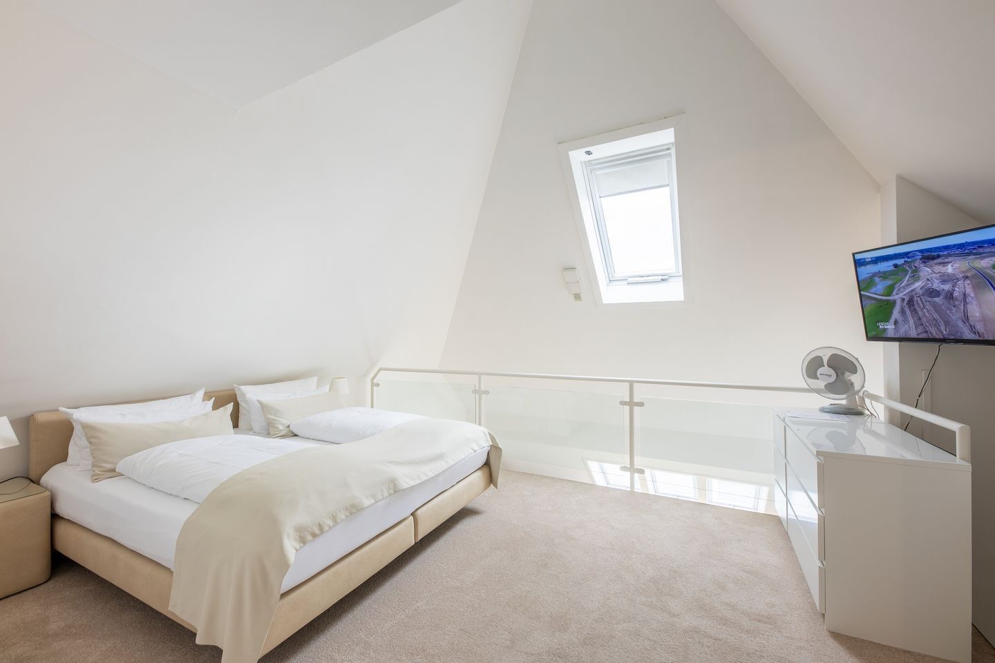 Ein Schlafzimmer mit Bett, Fernseher, Schreibtisch und Balkon.