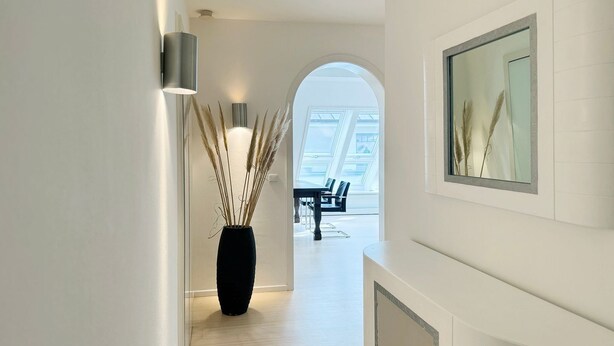 Ein moderner Flur mit einer schwarzen Vase mit Pampasgras, ein Essbereich mit Tisch und Stühlen sowie ein großes Fenster für natürliches Licht.