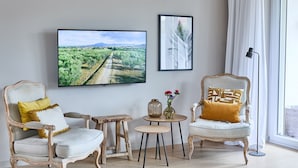 A living room with two ornate chairs, a small round table, and a large flat-screen TV mounted on the wall. - Apartment "Seestern" - Stylish retreat with terrace and beautiful view (Timmendorfer Strand)