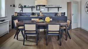 A modern kitchen with dark cabinetry, a central island, and a dining area with a wooden table and rattan chairs. - Apartment "Seestern" - Stylish retreat with terrace and beautiful view (Timmendorfer Strand)
