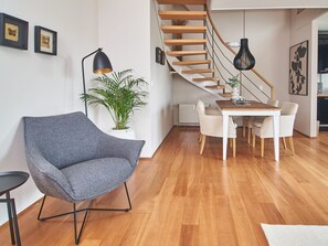 Uma sala de estar moderna com uma poltrona cinza, uma mesa de jantar com cadeiras, uma escada e um vaso de planta.
