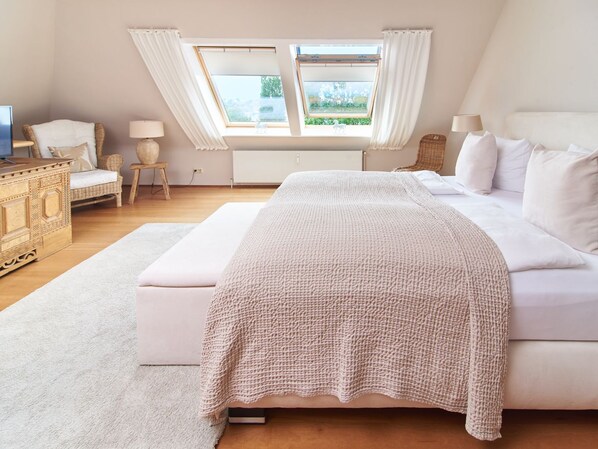 A bedroom with a large bed, a small side table, a chair, a dresser, and a window with curtains.