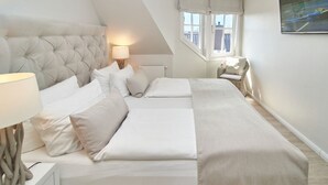Ein Schlafzimmer mit einem gesteppten Kopfteil, einer Nachttischlampe, einem großen Fenster mit Vorhängen und einem Bild an der Wand.