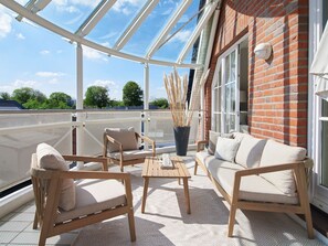 A covered outdoor seating area with a table and chairs, a potted plant, and a brick wall. - "Morgenstern" Penthouse—Light, Space, and Well-Being Above the Baltic Sea—TECHTs (Timmendorfer Strand)