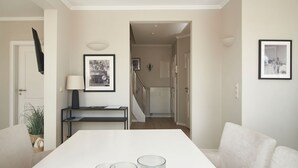 Ein modernes Wohnzimmer mit einem weißen Sofa, einem Esstisch mit Kerzen und einer Treppe, die in einen weiteren Raum führt.
