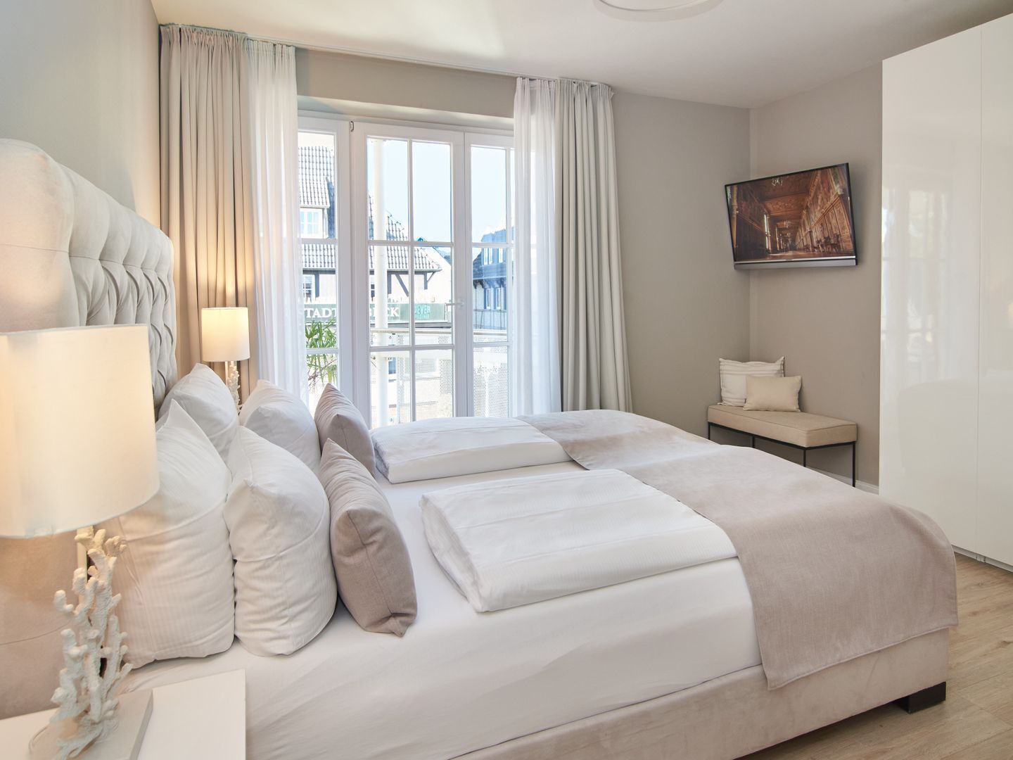 A hotel room with a bed, a nightstand, a lamp, a window with curtains, and a painting on the wall.