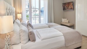 A hotel room with a bed, a nightstand, a lamp, a window with curtains, and a painting on the wall.