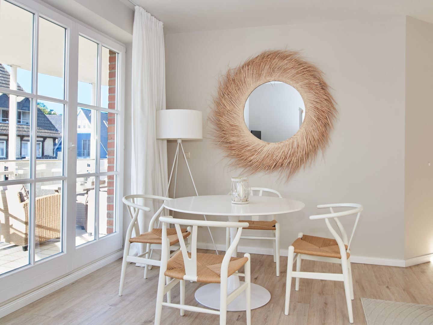 A room with a round mirror, a white table with four chairs, and a large window with curtains.