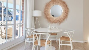 A room with a round mirror, a white table with four chairs, and a large window with curtains.