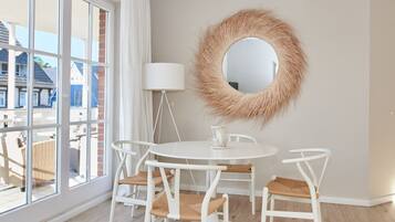 A room with a round mirror, a white table with four chairs, and a large window with curtains.