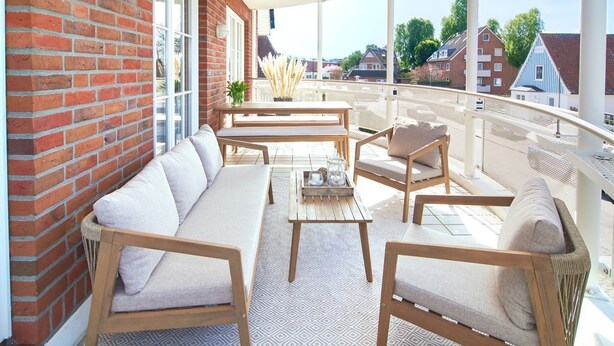 A balcony with a sofa, chairs, and a table, overlooking a residential area.