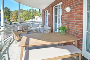 A balcony with a wooden table and chairs, a potted plant, and a view of the surrounding area. - Welcome to TECHTS - TECHTs Strandhaus (Timmendorfer Strand)