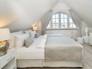 A bedroom with a large bed, two bedside tables with lamps, a window with curtains, and a view of buildings outside. - Apartment "SternenMeer" - Penthouse above the rooftops of Timmendorfer Strand - (Timmendorfer Strand)