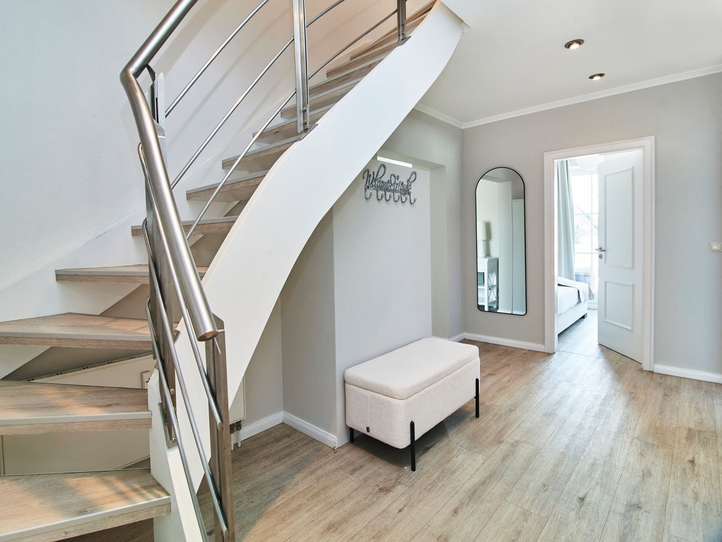 Ein modernes Interieur mit einer Wendeltreppe, einer Bank, einem Spiegel und einem Gang zu einem anderen Raum.