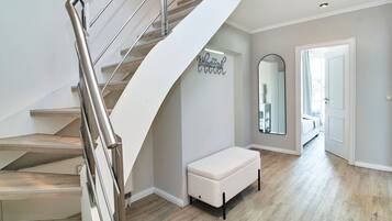 A modern interior with a spiral staircase, a bench, a mirror, and a hallway leading to another room.