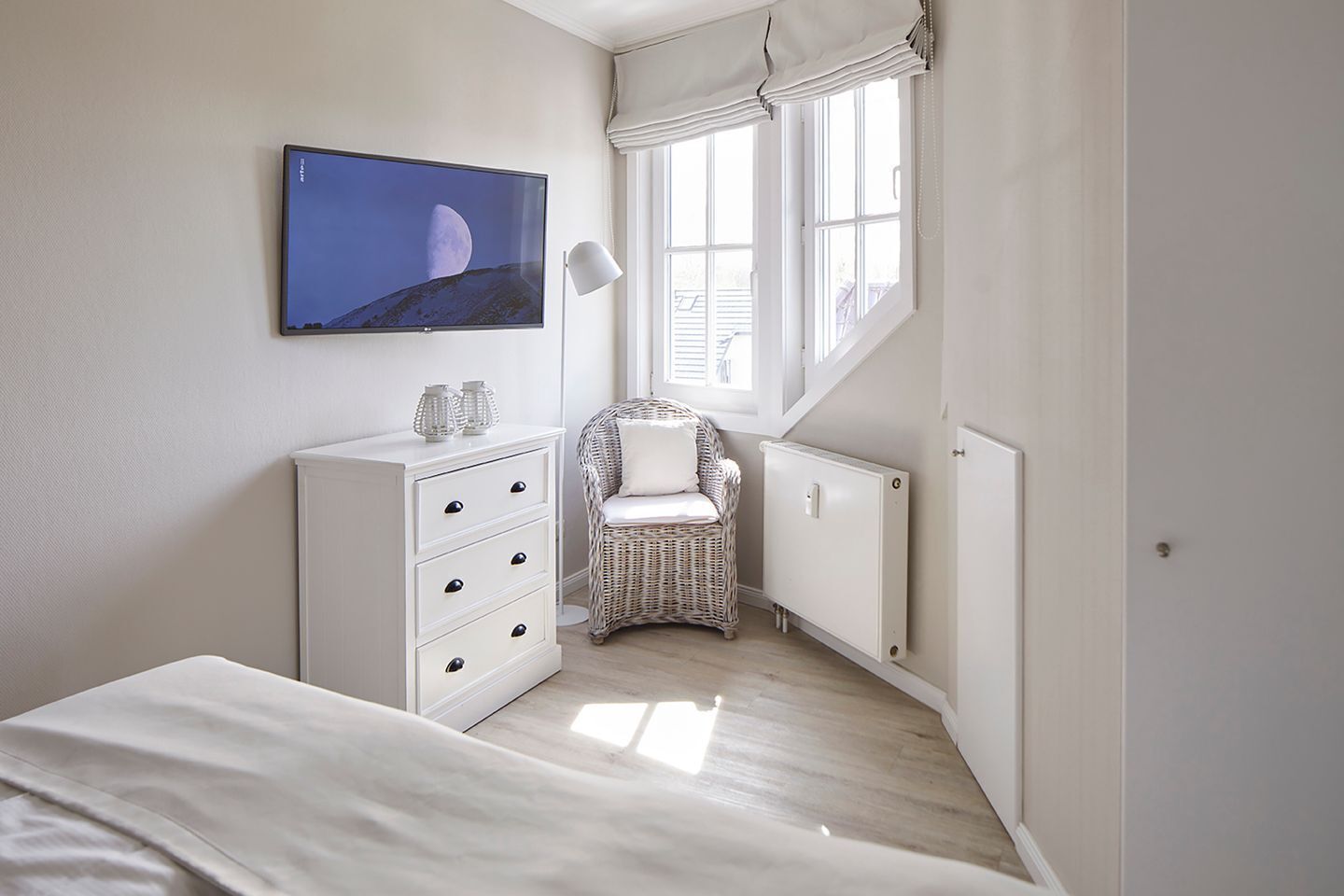Un dormitorio con una cama, un aparador, una silla, un radiador y un televisor en la pared.