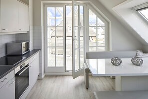 A modern kitchen with a large window, white cabinetry, and a dining area with a table and two decorative spheres. - Apartment "SternenMeer" - Penthouse above the rooftops of Timmendorfer Strand - (Timmendorfer Strand)