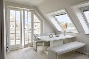 A modern room with a white bench, a table with decorative items, and large windows offering a view of buildings outside. - Apartment "SternenMeer" - Penthouse above the rooftops of Timmendorfer Strand - (Timmendorfer Strand)