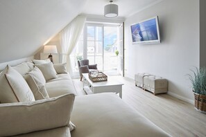 A modern living room with a sofa, a coffee table, a chair, a TV, and a window with a view. - Apartment "SternenMeer" - Penthouse above the rooftops of Timmendorfer Strand - (Timmendorfer Strand)