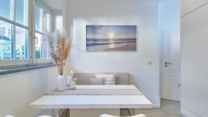 A modern dining area with a white table, two chairs, a painting of a beach scene, and a vase with dried plants. - Welcome to TECHTS - TECHTs Strandhaus (Timmendorfer Strand)