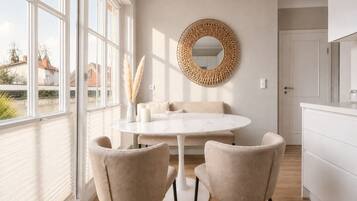A modern dining area with a round table, two chairs, a decorative mirror, and a view of the outside.