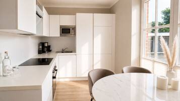 A modern kitchen with white cabinetry, a built-in microwave, and a dining area with a marble table and chairs.
