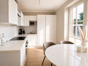 A modern kitchen with white cabinetry, a built-in microwave, and a dining area with a marble table and chairs. - A Love for the Coast – The Baltic Sea Up Close - TECHT's Beach House (Timmendorfer Strand)