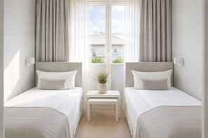 Ein Hotelzimmer mit zwei Einzelbetten, einem kleinen Tisch mit einer Pflanze und Blick auf Gebäude durch das Fenster.