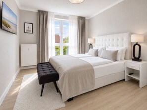 Een moderne slaapkamer met een groot bed, nachtlampen, een bankje en uitzicht op de omgeving.